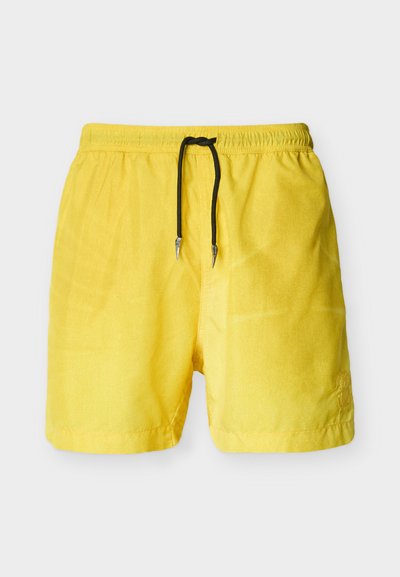 Κίτρινα ανδρικά μαγιό σορτς με ελαστική μέση και μαύρο κορδόνι, εμφανίζονται μπροστά σε απλό ανοιχτό γκρι φόντο.