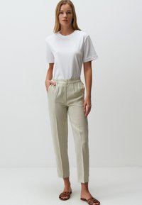 Hellbeige, hochgeschnittene Hose mit Knopfverschluss und elastischem Bund, kombiniert mit einem klassischen weißen T-Shirt aus Baumwolle.