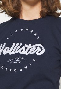 Camiseta de color azul marino hecha de algodón, con el logotipo bordado en blanco de "Hollister" y el texto "Southern California" en un diseño circular.
