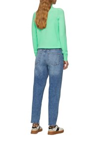 Lichtgroene sweater, blauwe denim jeans en beige sneakers. De sweater heeft lange mouwen; de jeans zijn iets taps toelopend en van gemiddelde hoogte.