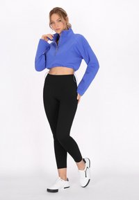 Korta, zip-upp jacka i klar blå, kombinerad med högmidjade svarta leggings och vita sneakers. Slät textur med dragsnoddselement.