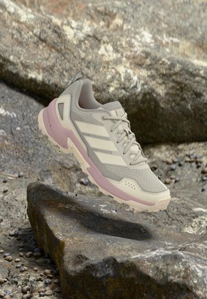 Beige og mauve Adidas sneaker med mesh og syntetisk overdel, svævende over stenet terræn med ru sten i baggrunden.