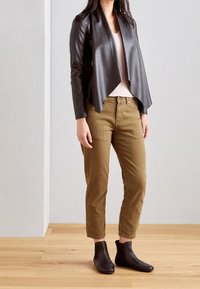 Veste courte en cuir noir avec devant drapé, haut côtelé rose clair, pantalon ajusté vert olive et bottines noires.