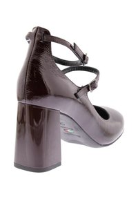 Scarpa con tacco alto bordeaux scuro, con finitura lucida in vernice, punta arrotondata, cinturini alla caviglia e tacco a blocco. La suola presenta un marchio e un dettaglio a bandiera.
