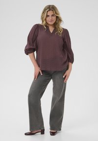 Maroon blouse with a V-neck and three-quarter puff sleeves, featuring a textured pattern. Paired with gray wide-leg jeans and dark shoes.