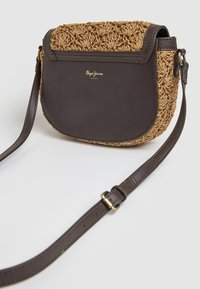 Kompaktowa torba na ramię z brązowym skórzanym dnem oraz plecioną górą z naturalnych włókien, ozdobiona złotym logo. W zestawie regulowany pasek.