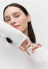 Witte langlee T-shirt met een aansluitende pasvorm, voorzien van duimgaten in de manchetten. De stof lijkt zacht en glad met minimale textuur.