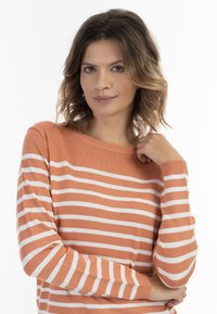 Oranžinė ir balta dryžuota megzta palaidinė su apvalia iškirpte, ilgomis rankovėmis ir minkšta tekstūra, turinti lygiai horizontalius dryžius.