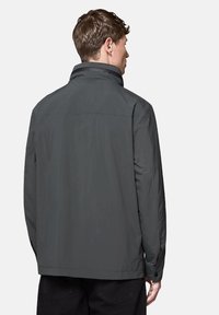 Szara zewnętrzna kurtka z wysokim kołnierzem, gładką powierzchnią i zapinanymi mankietami. Widok z tyłu ukazuje prosty krój o minimalistycznym designie.