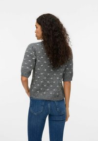 Grå kortärmad tröja med en fluffig textur och vita prickar; har en rundad halsringning och en rak passform, tillsammans med blå jeans.
