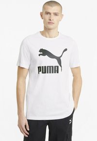 Hvid bomulds t-shirt med et stort sort Puma logo design. Kortærmet og rund hals med en afslappet pasform. Glat tekstur.