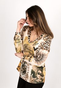 Silk blouse featuring a mix of an animal print and artistic patterns in gold, beige, and black, with a V-neckline and long sleeves.