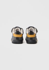 Scarpe per bambini con una tomaia grigia e nera, accenti gialli e blu, suole testurizzate e cinturini in Velcro per una calzata sicura.