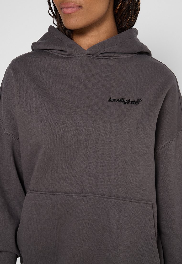 Osoba ubrana w ciemnoszary sweatshirt z kieszenią z przodu i małym czarnym logo "lawlights" na lewej piersi, widoczne warkocze.