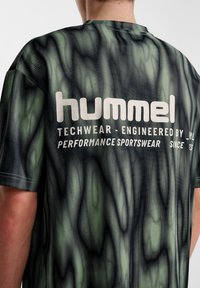 Grön och svart mönstrad techwear t-shirt med lös passform, med en stor vit logotyp på baksidan och ett slätt, texturerat tyg.