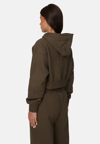 Hoodie court en vert olive foncé, fabriqué en tissu doux. Doté d'une capuche, de manches larges et d'une coupe décontractée. Associé à un pantalon de jogging assorti.