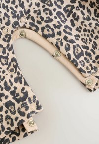 Leopardenmuster-Stoff mit beigem Hintergrund; verfügt über mehrere Druckknöpfe entlang des Randes; weiches, strukturiertes Material.