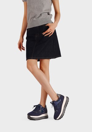 Jupe en denim foncé à coupe droite, associée à des baskets bleu marine avec des accents texturés et une semelle en caoutchouc blanc.