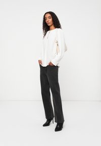 Witte lange mouwen top met een sleutelgatdetail, gecombineerd met zwarte rechttoe-rechtaan jeans en zwarte puntige hakken. Eenvoudige, gladde textuur.