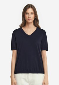 Marinblå kortärmad V-ringad tröja, tillverkad av mjukt stickat material, med rullade ärmslut och lös passform, samt en rak nederkant.