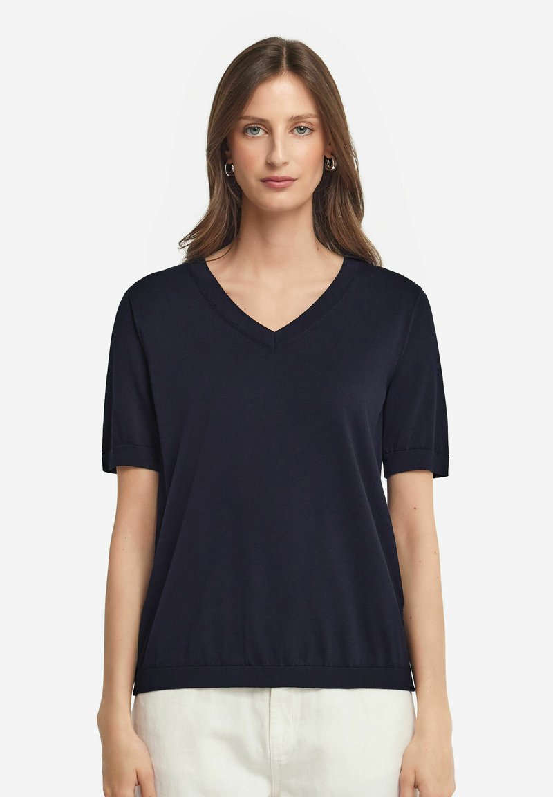 Marinblå kortärmad V-ringad tröja, tillverkad av mjukt stickat material, med rullade ärmslut och lös passform, samt en rak nederkant.