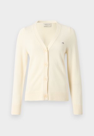 Cremfarbener Cardigan aus weichem Strickmaterial, mit V-Ausschnitt, fünf Knöpfen, gerippten Bündchen und einem kleinen Logo auf der linken Seite.