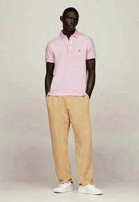 Heleroosa lühikeste varrukatega polo ja kaelusega, kombineeritud beežide, lõdvalt istuvate pükstega ning valgete tennistega.