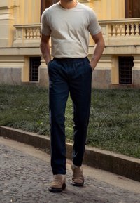 Beige bomull t-shirt och byxor med marinblå elastisk midja. Byxorna har en avslappnad passform och är kombinerade med ljusbruna slip-on skor. Urban miljö.