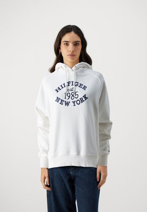 Felpa bianca con un stampa frontale che recita "HILFIGER est 1985 NEW YORK" in blu navy. Presenta un cappuccio con cordino e polsini a coste. Realizzata in morbido misto cotone.