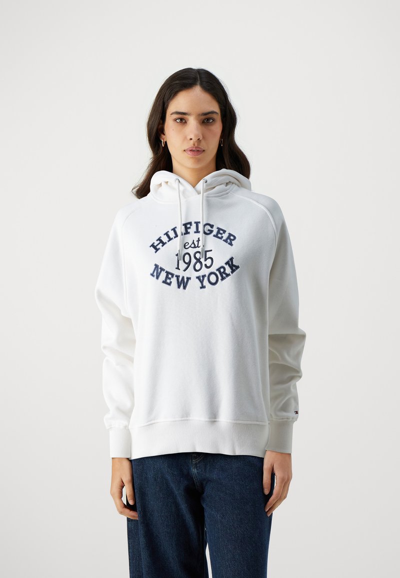 Felpa bianca con un stampa frontale che recita "HILFIGER est 1985 NEW YORK" in blu navy. Presenta un cappuccio con cordino e polsini a coste. Realizzata in morbido misto cotone.