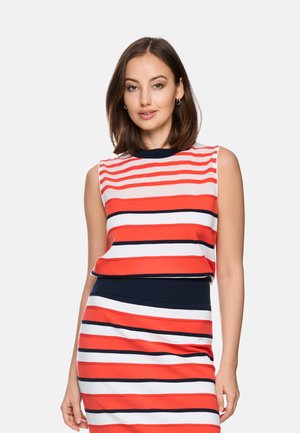 Woman with shoulder-length brown hair wearing a sleeveless red, white, and navy striped top and matching skirt against a plain background.