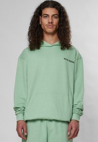 Myntgrön hoodie med känguruficka, ribbade muddar och en broderad logotyp. Mjuk tyg med avslappnad passform.