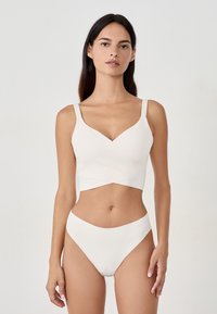Bralette bianca con scollatura a V e design incrociato, abbinata a slip a vita alta coordinati. Texture liscia e design minimalista.