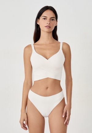Brassière blanca con escote en V y diseño entrelazado, combinada con braguitas de talle alto a juego. Textura suave y diseño minimalista.