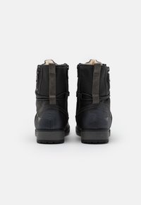 Para czarnych skórzanych butów za kostkę z szarymi uchwytami, zamkami bocznymi i widoczną od góry wyściółką z owczej wełny, widziana z tyłu.