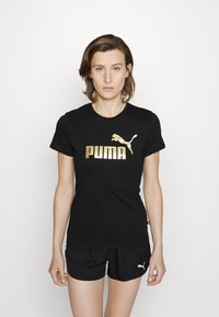Black t-shirt made of cotton with a gold "PUMA" logo and leaping puma graphic. Paired with black shorts featuring a small white logo.