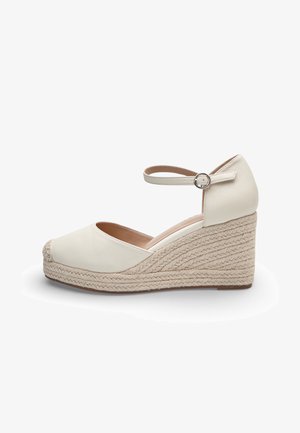 Espadrilla beige da donna con zeppa, cinturino alla caviglia e suola intrecciata in juta, punta chiusa e chiusura con fibbia su sfondo bianco neutro.
