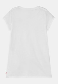 Camiseta blanca de algodón con mangas cortas y cuello redondo. Presenta un diseño sencillo, textura suave y un pequeño logotipo rojo en el dobladillo.
