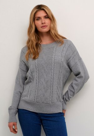Grå strikket sweater med kabelstrik mønster, rund halsudskæring og ribbede manchetter og kant. Bæres med blå jeans. Blød tekstur, boxy pasform.