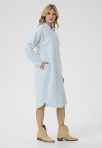 Blå och vit randig skjortklänning med långa ärmar, med sidofickor och rundad nederkant, tillsammans med beige ankelskor.