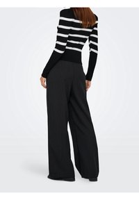 Haut à manches longues rayé noir et blanc, associé à un pantalon large noir à fines rayures. Le tissu semble doux, avec une taille cintrée.