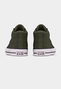 Kaheksa kõrge säärega oliivrohelised Converse All Star tennised, vaadatuna tagantpoolt valgel taustal.