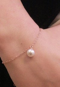 Bracciale a catena in oro rosa con un singolo pendente di perla bianca rotonda; texture liscia, design delicato, adatto per un abbigliamento casual o formale.
