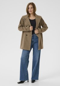 Brauner Wollmischmantel mit breitem Kragen und doppelter Knopfleiste, kombiniert mit dunkelblauen weit geschnittenen Jeans und schwarzen Heels.