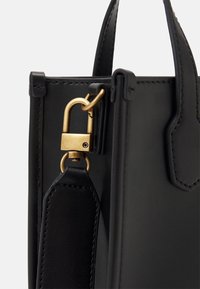 Czarna skórzana torebka z kątem, wyposażona w zapięcie ze złotym okuciem, gładką teksturę, dwa uchwyty oraz odpinany pasek z detalami przeszycia.