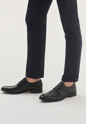 Czarne skórzane buty do garnituru z podwójnymi zapięciami; elegancki design i gładka tekstura; zestawione z granatowymi spodniami, skróconymi na kostkach.