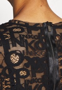 Black lace top featuring a mesh design with embossed letters, exposing skin underneath. Zipper closure at the back with a satin accent.