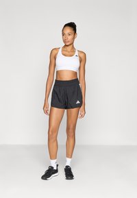 Λευκό αθλητικό σουτιέν, μαύρο σορτς με ελαστική μέση, με λογότυπο, φορεμένα με μαύρα αθλητικά παπούτσια και λευκές κάλτσες αστραγάλου.