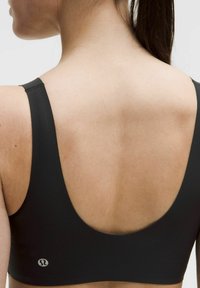 Sujetador deportivo negro con un diseño de espalda baja, hecho de material suave y elástico. Cuenta con tirantes anchos y un pequeño logo en la parte inferior izquierda.