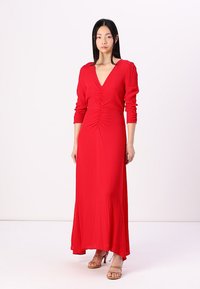 Robe rouge à manches longues présentant un décolleté en V profond et des détails froncés à la taille. Le tissu lisse et l'ourlet évasé mettent en valeur la silhouette.